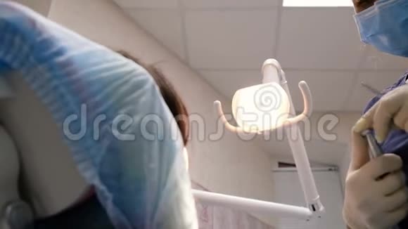 年轻的女牙医正在给病人治疗和钻孔牙齿在口腔医生那里接受治疗视频的预览图