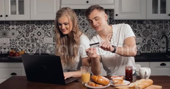 年轻夫妇在厨房的笔记本电脑网上购物视频的预览图