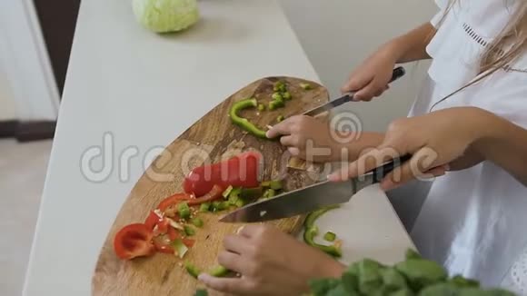 厨房桌子上砧板的俯视图女人的手把青椒和红椒切成两半作为蔬菜视频的预览图