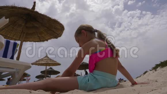 坐在度假胜地海滩上在多云的天空中倾斜的女孩视频的预览图