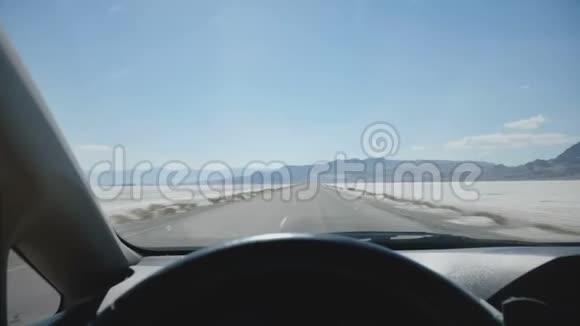 一辆车正沿着史诗般的白色盐湖沙漠公路驶向群山和晴空地平线公路旅行的概念视频的预览图