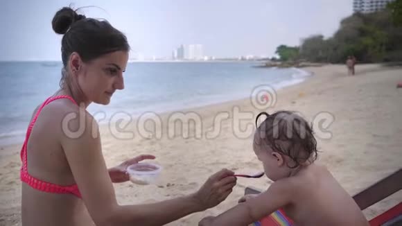 妈妈在海滩上用勺子喂女儿特写镜头4K视频的预览图