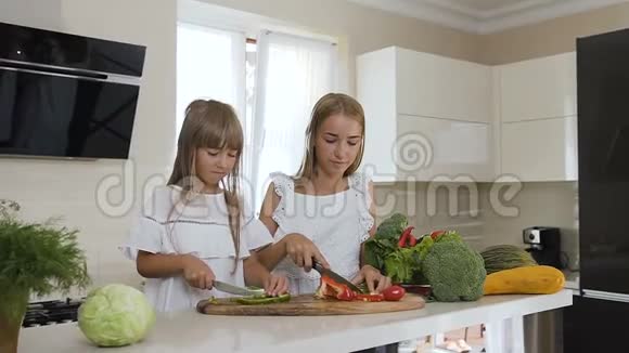 一对白衣长发的姐妹正在现代厨房的木凳上切新鲜蔬菜吸引人视频的预览图