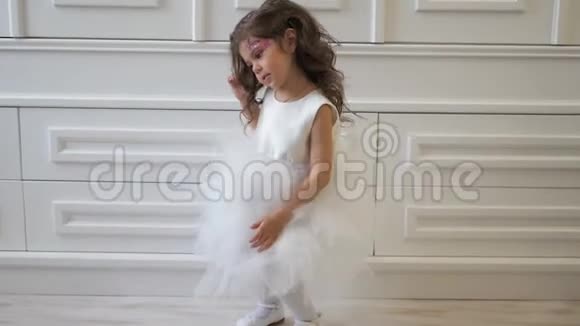 小女孩穿着华丽的白色连衣裙在室内做着闪亮的化妆和发型在室内跳舞视频的预览图