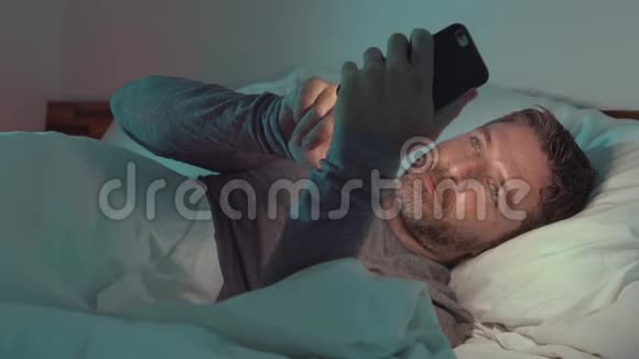 一个年轻有魅力爱睡懒觉的人在床上用手机上的社交应用程序视频的预览图