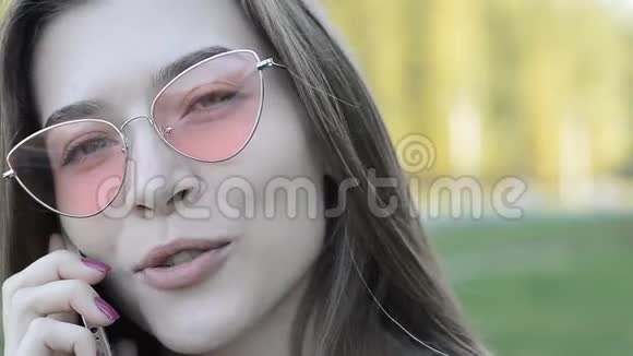 一位身穿粉色太阳镜的年轻美女在公园打电话的特写镜头视频的预览图
