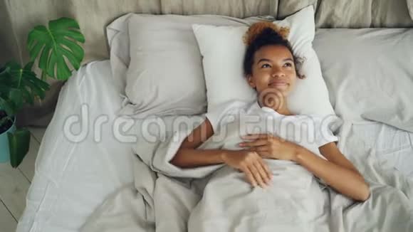 快乐的混血女孩躺在床上微笑然后伸展手臂闭上眼睛睡着了安息的人视频的预览图