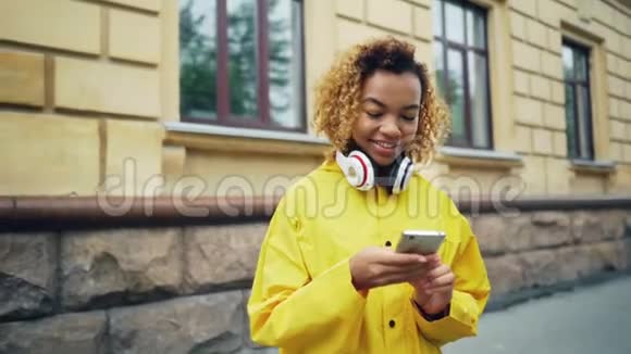 快乐的非裔美国学生正在使用智能手机浏览或短信朋友站在户外的现代街道上视频的预览图