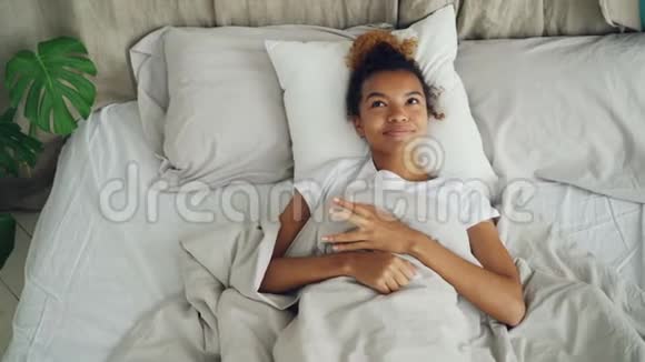 幸福的年轻女子躺在床上醒着微笑着享受无忧无虑的生活舒适的床和好消息积极正面视频的预览图