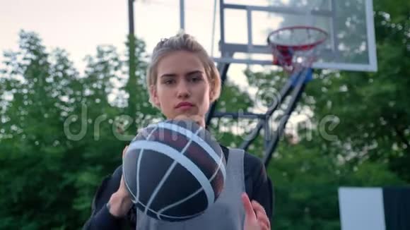 漂亮的金发女郎把篮球对准镜头职业球员白天站在公园里呼噜呼噜地叫着视频的预览图