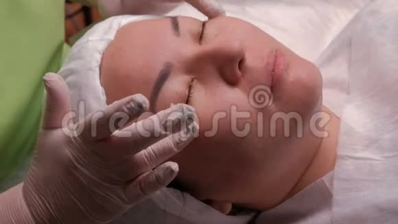 一个亚洲女孩在美容院的面部按摩在手术过程中在白色手套中密切美容师的手视频的预览图