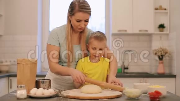 那个漂亮的金发小男孩帮妈妈做饭妈妈和儿子穿着五颜六色的衬衫正在把面团卷出来妈妈是视频的预览图