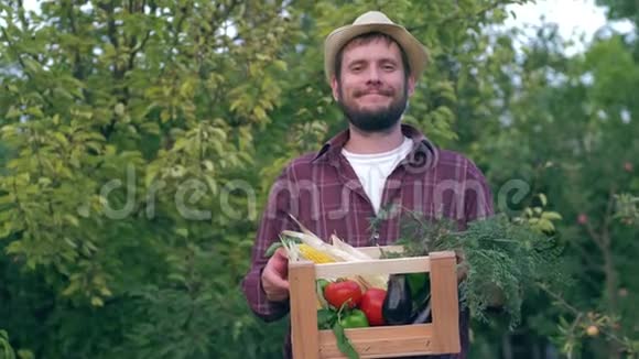 农贸市场戴着草帽的高兴男子拿着装有有机新鲜蔬菜的木箱在户外出售视频的预览图