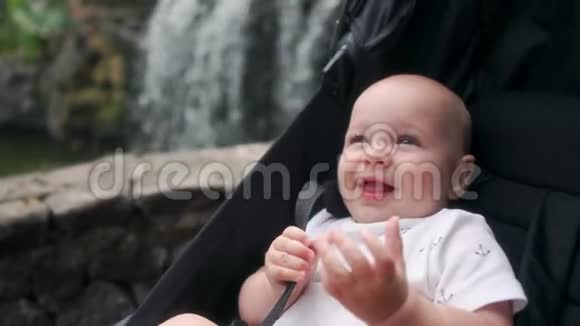 婴儿坐在瀑布附近的轮椅上笑着看着相机在remsa和父母一起旅行视频的预览图