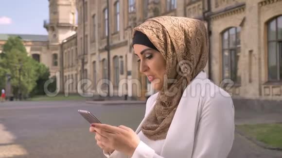 美丽快乐的穆斯林女人戴着头巾打电话站在街上背景是建筑商务女士视频的预览图
