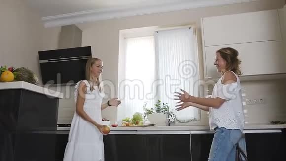 穿着白色衣服的漂亮女孩在厨房里给对方扔一个大绿苹果时玩得很开心视频的预览图