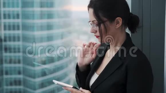 年轻女子站在摩天大楼的高楼层上使用智能手机视频的预览图