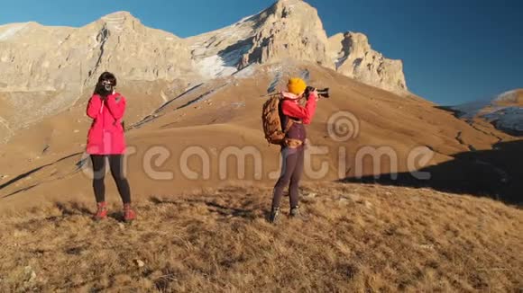 两个带背包和照相机的旅行女孩在山上漫步在史诗般的岩石之间的空中景色视频的预览图