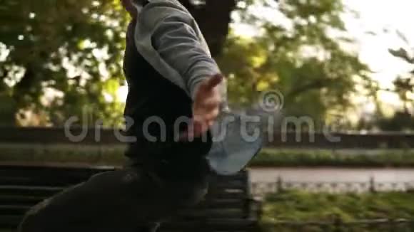 快乐的年轻人戴着黑色耳机在公园里骑自行车伸出双手的人享受在户外视频的预览图