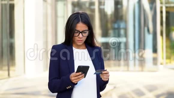 年轻漂亮的商业女性或学生使用银行她的智能手机在办公楼背景网上在线视频的预览图