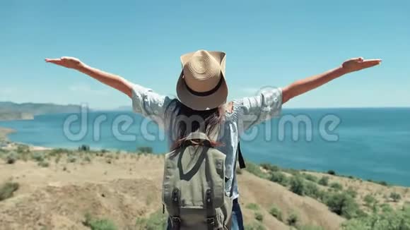 中镜头活跃的女旅行者戴着太阳镜和帽子欣赏海景举手视频的预览图