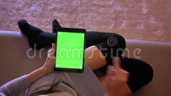 在平板电脑上用绿色屏幕特写年轻漂亮女性网络的肖像女孩的腿在舒适的位置视频的预览图