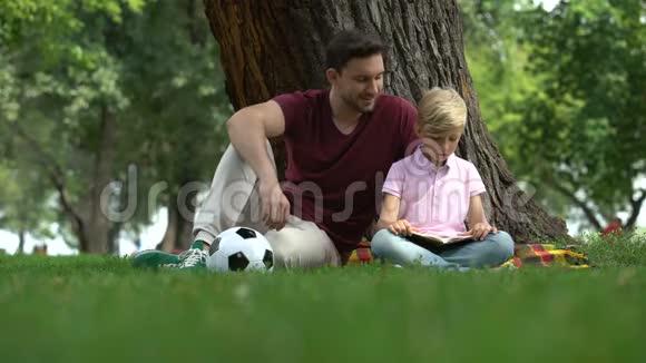父亲和儿子在公园看书男人鼓励男孩知识家庭视频的预览图