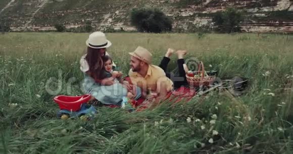 大自然中间和一个年轻的家庭一起野餐所有的成员都躺在毯子上互相抱着视频的预览图