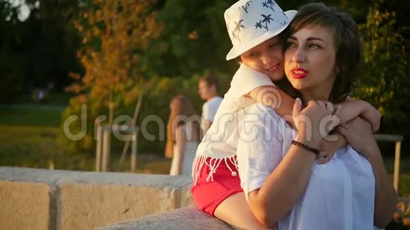 妈妈在她女儿旁边欣赏城市日落戴着可爱帽子的可爱的母女被傍晚的阳光照亮视频的预览图