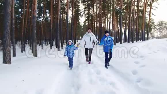 一位健康活跃的妇女带着两个孩子漫步在森林里白雪覆盖的道路上视频的预览图
