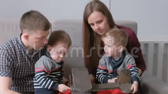 一家人的爸爸妈妈和两个双胞胎兄弟坐在沙发上玩木飞机视频的预览图