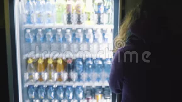 从穿紫色外套的年轻女人的背部看从自动售货机上选择饮料库存录像饮料自动售货机视频的预览图