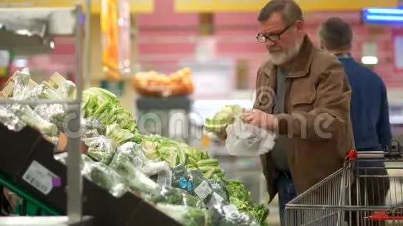 退休人员在超市购物一个男人挑选蔬菜做素食沙拉然后把它们放进手推车里视频的预览图