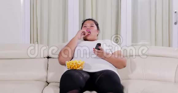 肥胖妇女一边吃爆米花一边看电视视频的预览图