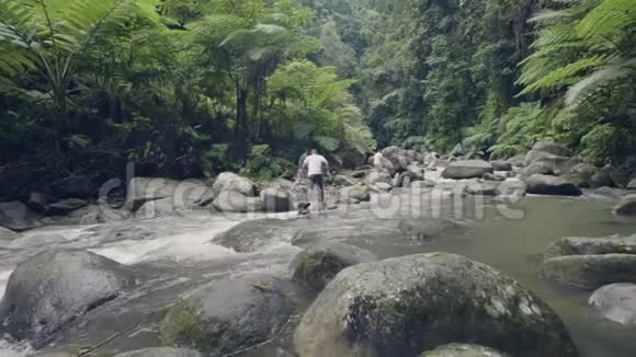 成群游客在雨林中流动的山河岩石上行走无人看人们在石头上旅行视频的预览图