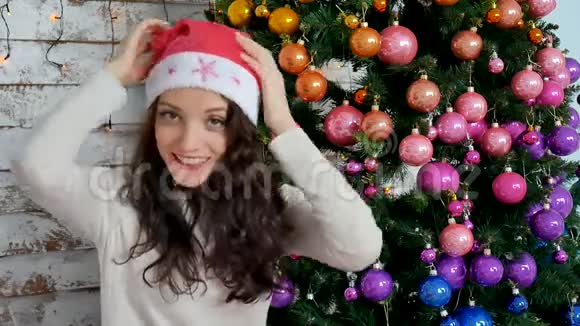 圣诞树旁戴圣诞帽的年轻女子视频的预览图