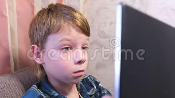 男孩看着坐在家里沙发上的电脑屏幕视频的预览图