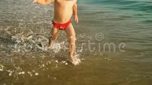 快乐的男孩快乐地跑着跳着在夕阳下溅在海水里慢动作视频的预览图