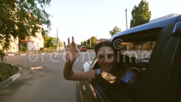 年轻漂亮的女孩乘着一辆车双手伸出窗外在市中心笑慢动作视频的预览图