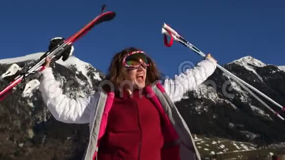 穿着滑雪服戴着镜子眼镜手里拿着滑雪板和滑雪杆的活跃女孩尖叫着投掷和胜利视频的预览图
