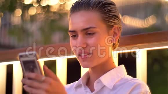 现代女性站在梯子上晚上在智能手机上看照片抽烟表情放松视频的预览图