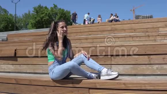 坐在公园长凳上用手机说话的女孩4K视频的预览图