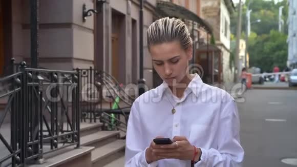 年轻的现代女性走在街上白天四处张望在智能手机上输入信息交流视频的预览图