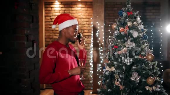 圣诞节一个英俊的男人带着一杯香槟在一个设计良好的客厅里打电话视频的预览图