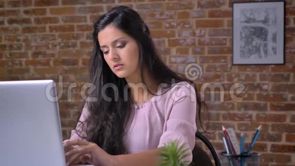 年轻的白种人女孩在阁楼办公室工作手提电脑打字看相机微笑背景砖墙视频的预览图