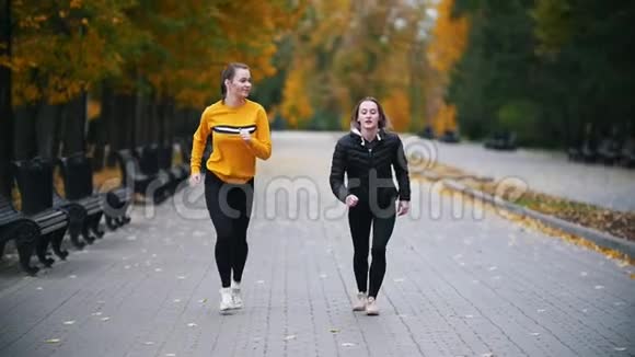 年轻健康的女人在秋天公园跑步朝镜头跑去慢动作视频的预览图