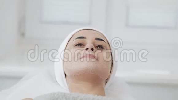 年轻漂亮的女人躺在沙发上在水疗美容院戴着白色面膜慢动作视频的预览图