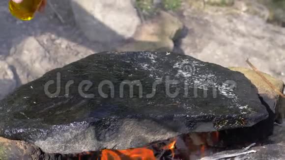 橄榄油倒在篝火上的热石上供野餐时户外烹饪食物视频的预览图