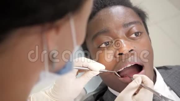 女牙医治疗病人年轻的非裔美国男性病人在牙科诊所的椅子上医学卫生视频的预览图