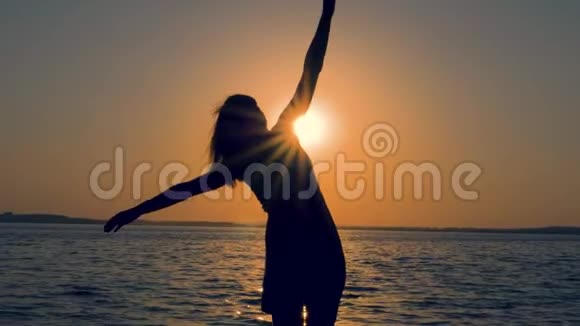 年轻女子的剪影在海上日落时举起双手侧着身子视频的预览图